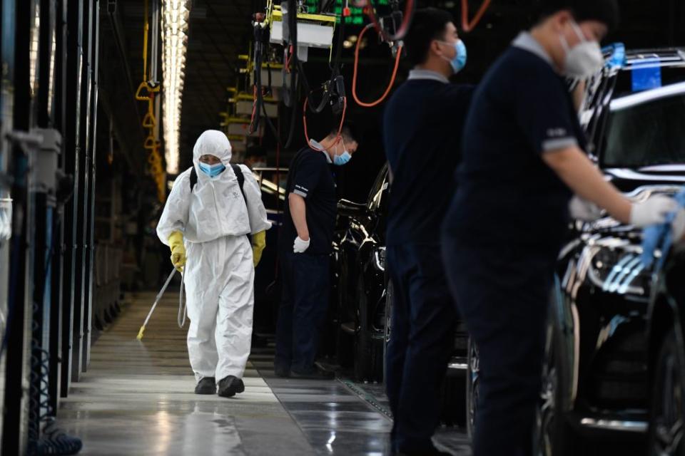 A cleaner wearing protective gear sprays disinfectant along a production line at a Mercedes Benz automotive plant during a media tour organised by the government in Beijing on May 13, 2020, as the country's industrial sector starts again following shutdowns during the COVID-19 coronavirus outbreak. | Wang Zhao/AFP via Getty Images