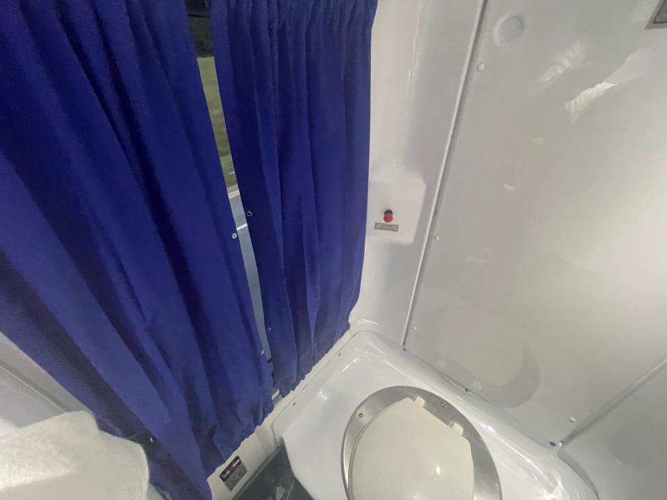 A bathroom on the Flixbus coach bus that has a plastic toilet and a curtain covering a window.