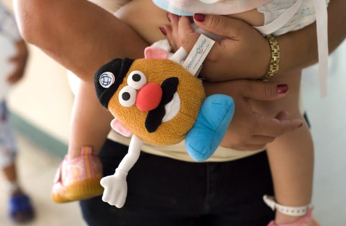 A woman's arms holding a small child and a plushie Mr. Potato Head.