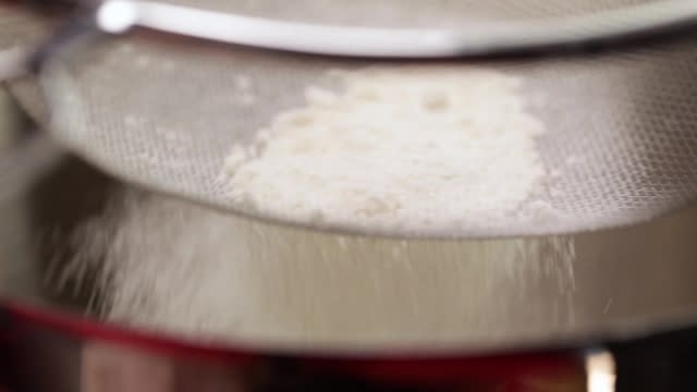 Sieving flour into a mixing bowl with a metal sieve