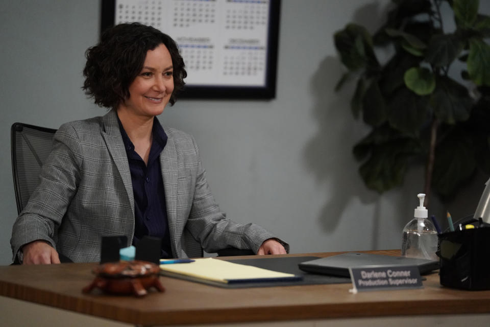 SARA GILBERT sits behind a desk