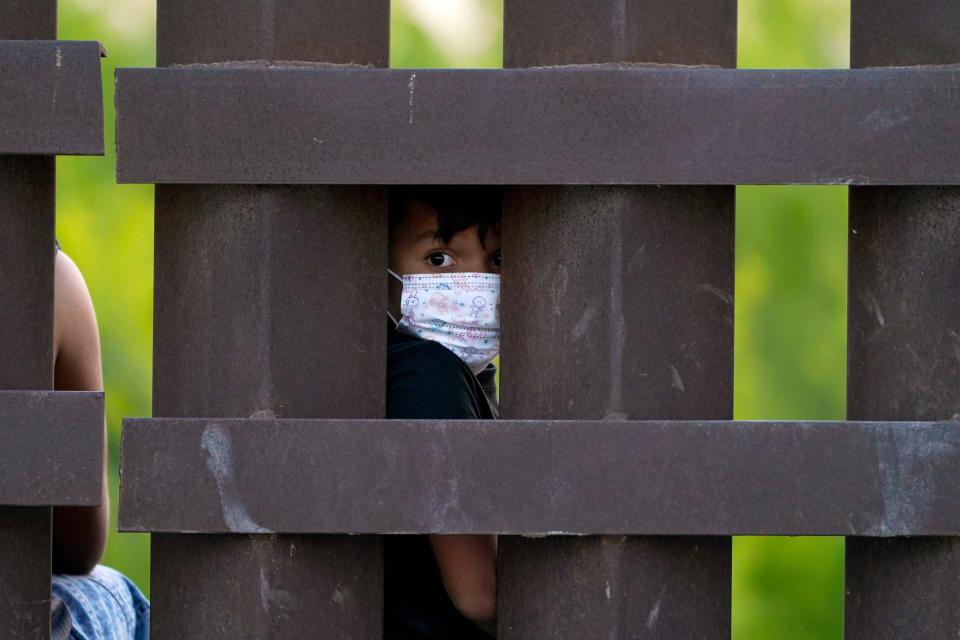 March 21, 2021: A migrant child looks through the U.S.-Mexico border wall as a group is processed and taken into custody while trying to sneak across the border in Abram-Perezville, Texas.