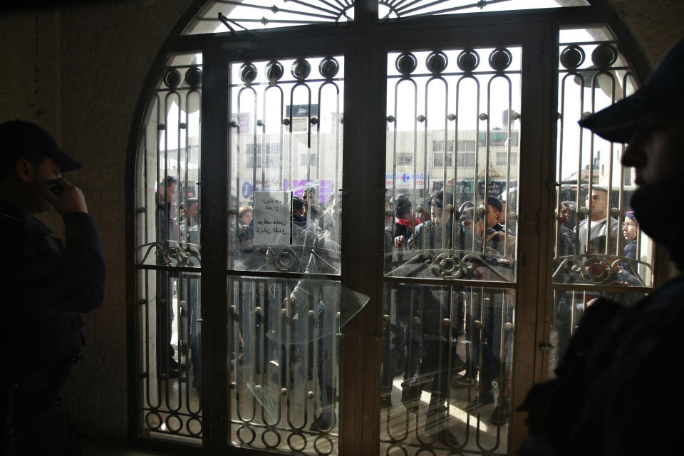 Palestinian protesters look through broken glass doors of a gate at a hotel where a group of Israelis and Palestinians hold a meeting in the West Bank city of Ramallah, Thursday, Jan. 9, 2014. Palestinians have thrown rocks at a West Bank hotel where Israeli and Palestinian peace activists were meeting. (AP Photo/Majdi Mohammed)