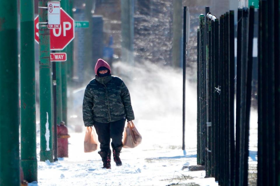 PHOTO: A person walk almost a half mile to their home from a grocery store as steam from an underground vent rises behind them in the Bronzeville neighborhood of Chicago, Jan. 16, 2024. (Charles Rex Arbogast/AP)