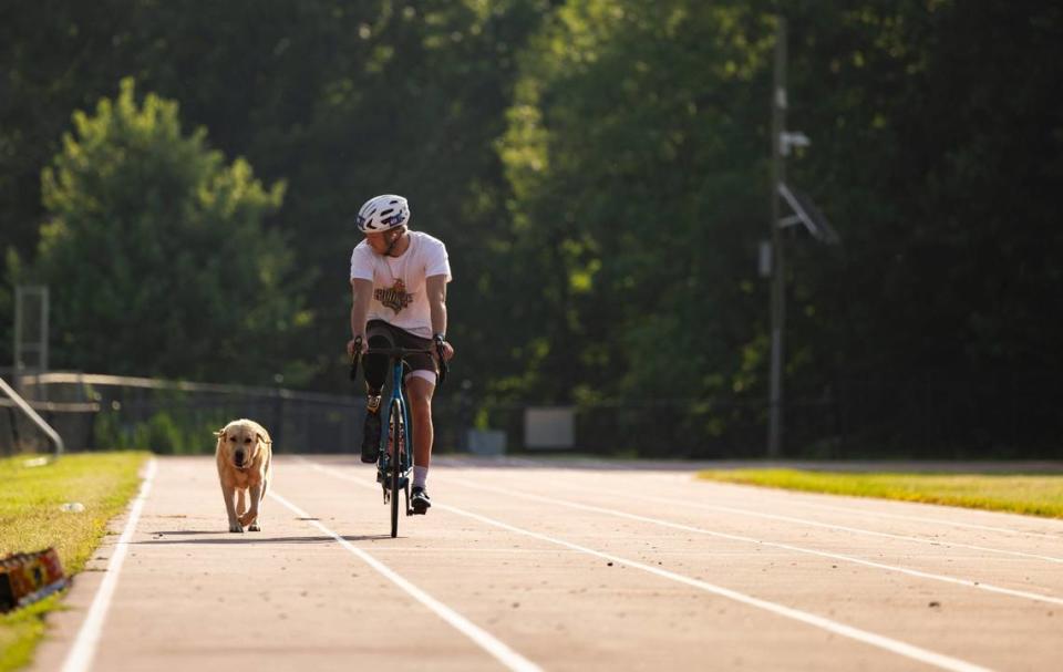 Carson Clough warms up on his bike while his service dog, Calder, tags along as he trains for the Paralympics triathlon at Alexander Graham Middle School in Charlotte, N.C., on Saturday, July 6, 2024.