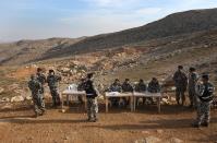 Lebanese General Security forces sit behind tables after they set up a temporary checkpoint to put an exit and entry stamps for the citizens who want to leave or enter the Tfail village at the Lebanese-Syrian border, eastern Lebanon, Tuesday April 22, 2014. A Lebanese convoy of soldiers, clerics and Red Cross officials delivered aid Tuesday to a remote village near the Syrian border that was bombed by Syrian government aircraft and blocked by Lebanese militants fighting alongside President Bashar Assad’s forces in the civil war next door. Hezbollah fighters have been patrolling the area on the Lebanese side and fighting has flared up inside Syria, cutting Tfail’s residents off from all sides for months. (AP Photo/Hussein Malla)