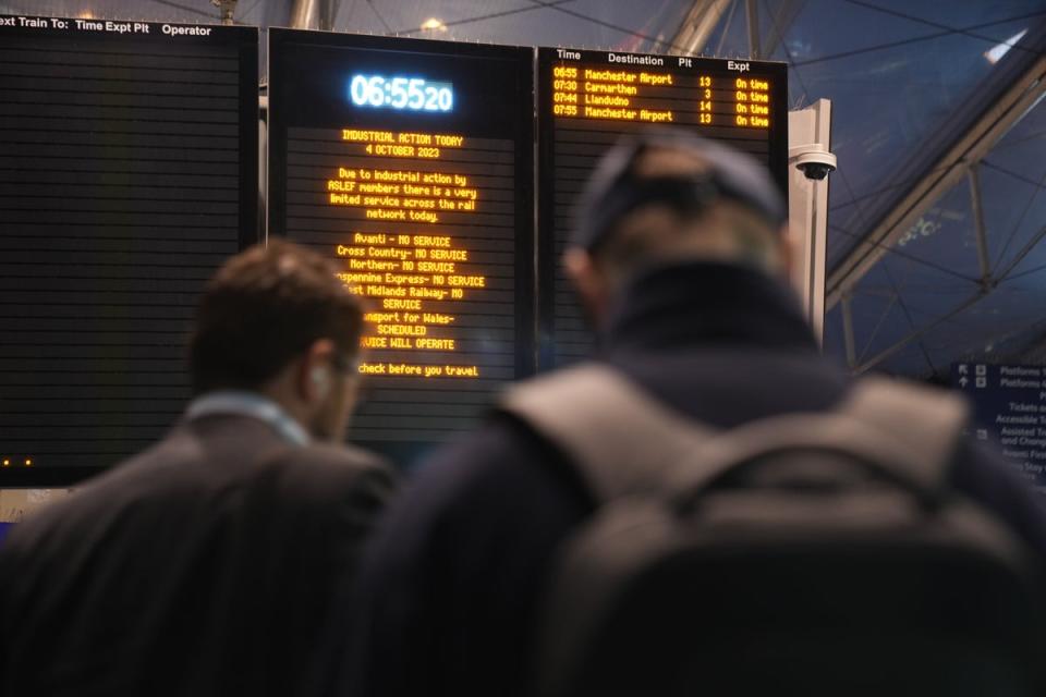 Commuters stand in front of an information sign detailing strike action at Manchester Piccadilly train station (PA) (PA Wire)