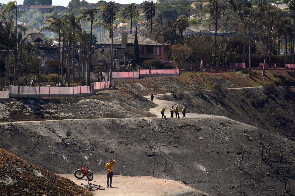 Firefighters and residents stand on a fire road where the Coastal Fire jumped and burned several homes Thursday, May 12, 2022, in Laguna Niguel, Calif. (AP Photo/Marcio Jose Sanchez)