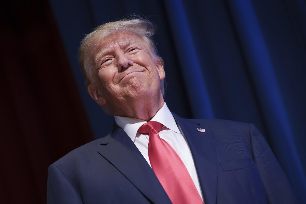 Former President Donald Trump stands in front of a curtain.