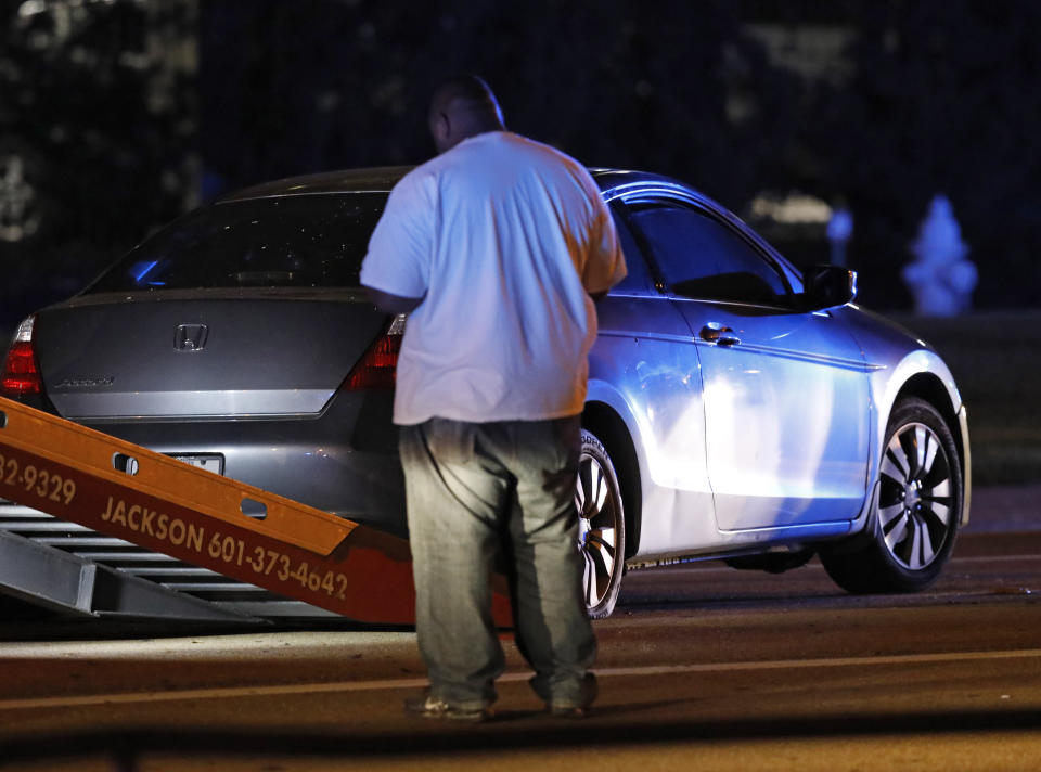 A wrecker service employee inspects a vehicle that is possibly involved in a shooting incident in front of the parking garage at the University of Mississippi Medical Center in Jackson, Miss., Thursday, Nov. 29, 2018. Two young children were shot Thursday in a car being driven by their mother near the University of Mississippi Medical Center, prompting the mother to pull them from the car and run them to the emergency room. (AP Photo/Rogelio V. Solis)