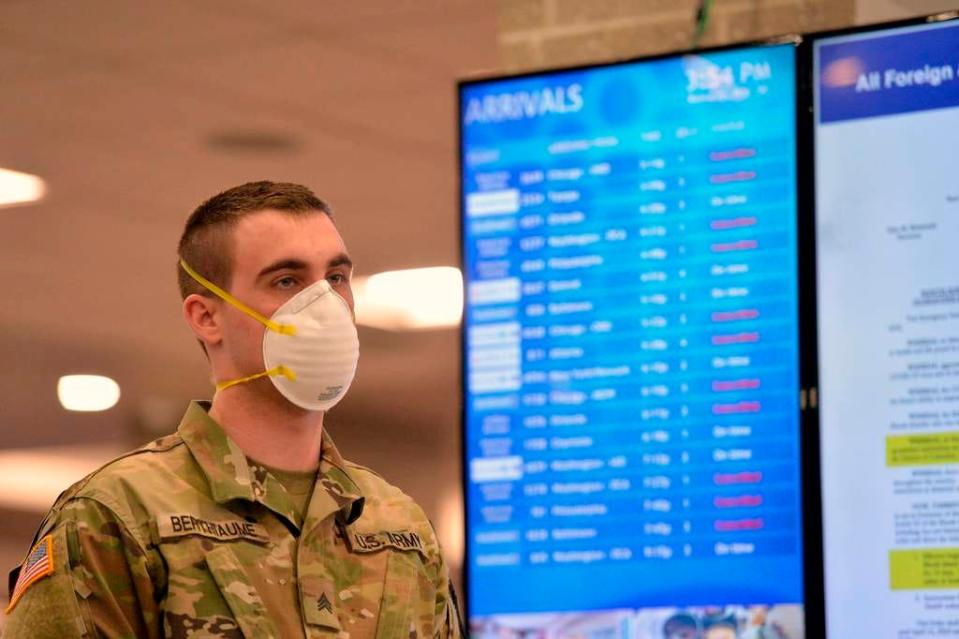 An Army National Guard soldier waits to inform those arriving at an airport in Warwick, Rhode Island, on March 30, 2020, of an order for all travelers to self-quarantine for 14 days.
