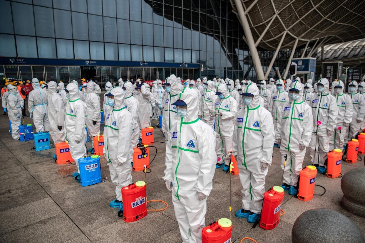 Staff members line up at attention as they prepare to spray disinfectant at Wuhan Railway Station: AFP via Getty Images