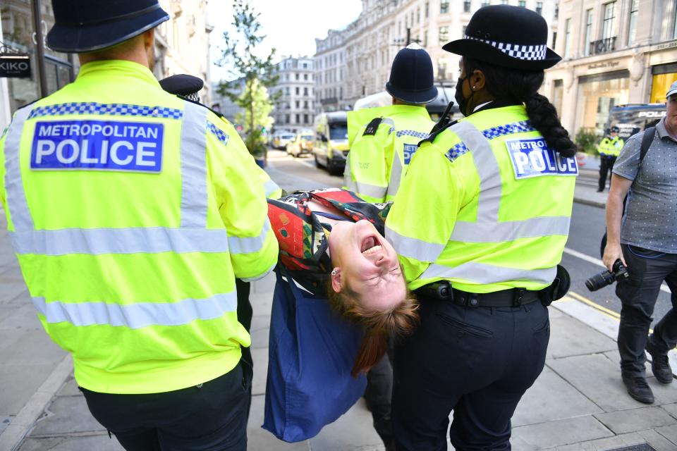 A climate activist from the Extinction Rebellion group is escroted away by police officers from a demonstration blocking the road in the middle of Oxford Circus in central London on August 25, 2021 during the group's 'Impossible Rebellion' series of actions. - Climate change demonstrators from environmental activist group Extinction Rebellion continued with their latest round of protests in central London, promising two weeks of disruption. (Photo by JUSTIN TALLIS / AFP) (Photo by JUSTIN TALLIS/AFP via Getty Images)
