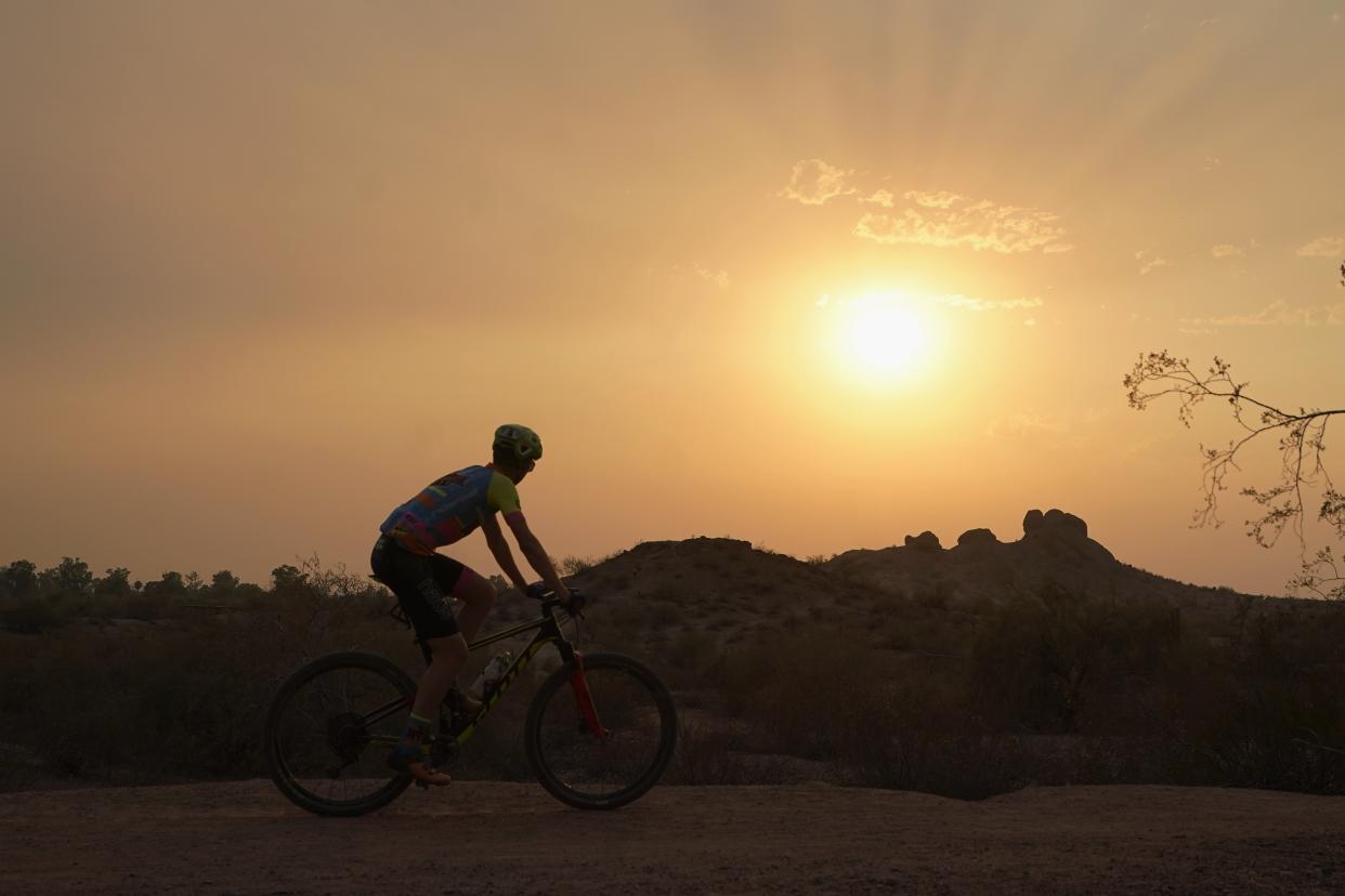 A cyclist bikes past the setting sun at Papago Park during a heatwave where temperatures hit 115-degrees Tuesday, June 15, 2021, in Phoenix. (AP Photo/Ross D. Franklin)