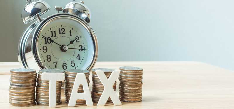 The word tax sits in front of stacks of coins and an alarm clock.