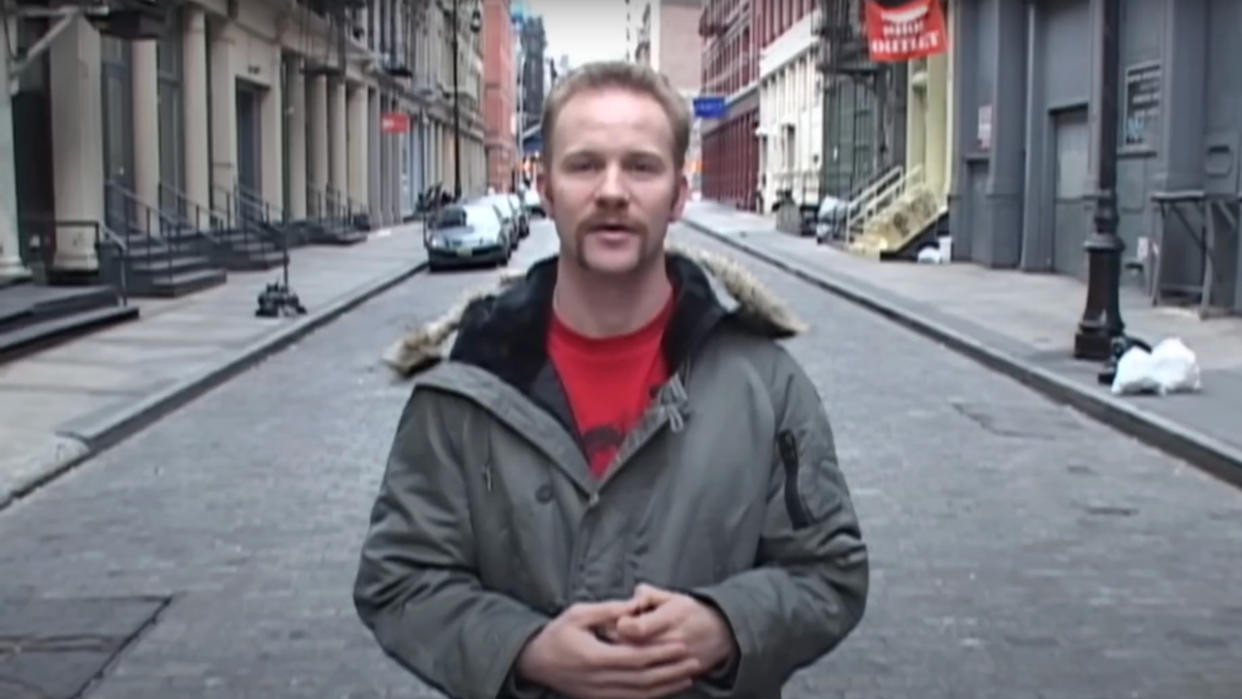  Morgan Spurlock speaking in the middle of the street, wearing a grey coat in Super Size Me. 