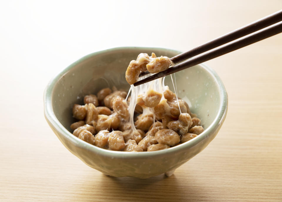 Natto in a plate set against a wooden background is lifted with chopsticks