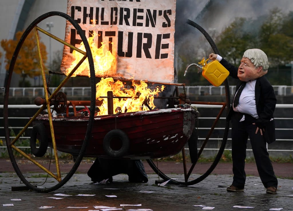 An Ocean Rebellion protester dressed as Prime Minister Boris Johnson sets fire to the boat sail (Andrew Milligan/PA) (PA Wire)