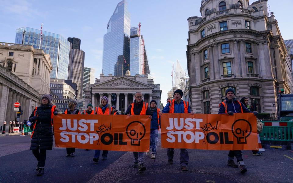 Ακτιβιστές του Just Stop Oil κρατούν πανό για να επιβραδύνουν την κυκλοφορία στην οικονομική περιοχή του City του Λονδίνου τον Δεκέμβριο του 2023