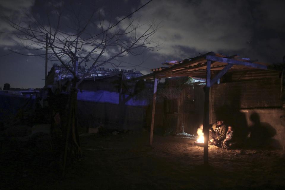 In this Sunday, Jan. 15, 2017 photo, a Palestinian family warm themselves up with a fire outside their makeshift house during the power cut in a poor neighborhood in town of Khan Younis in the southern Gaza Strip. At night, large swaths of the Gaza Strip plunge into darkness _ the result of chronic and worsening power outages. In crowded city streets, the only source of light comes from the headlights of passing cars. The power shortages are the worst to hit Gaza since Hamas seized control of the territory 10 years ago. (AP Photo/ Khalil Hamra)