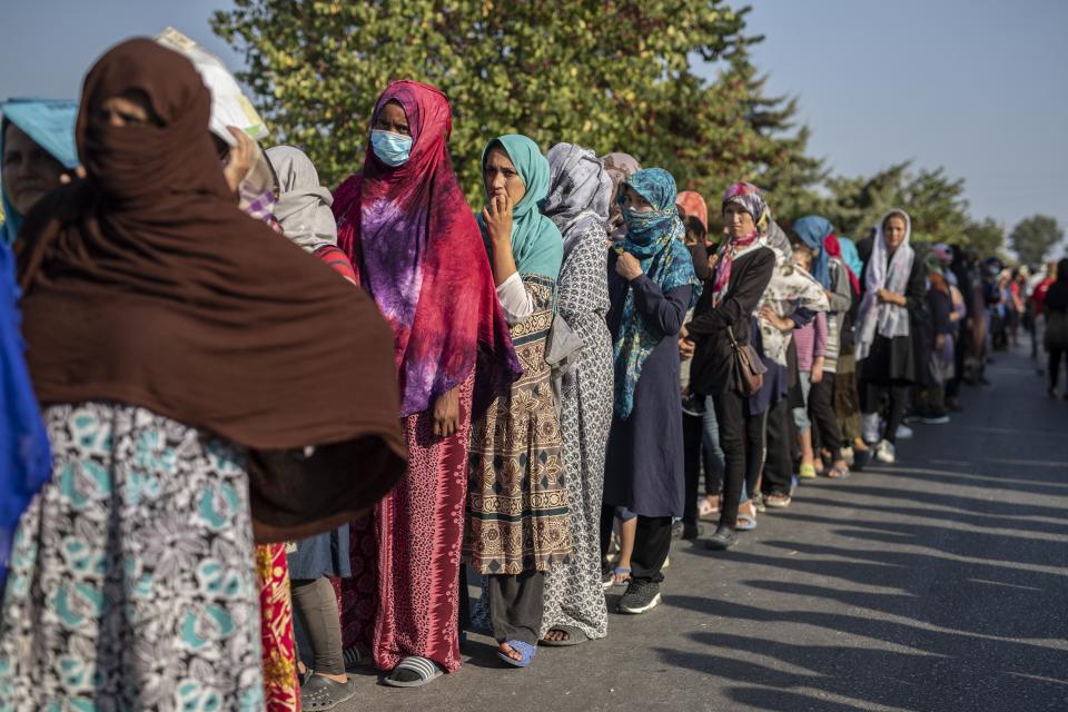 Migrants wait in a queue for food distribution near Mytilene town, on the northeastern island of Lesbos, Greece, Saturday, Sept. 12, 2020. Greek authorities have been scrambling to find a way to house more than 12,000 people left in need of emergency shelter on the island after the fires deliberately set on Tuesday and Wednesday night gutted the Moria refugee camp. (AP Photo/Petros Giannakouris)