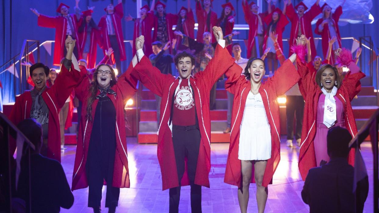  From left to right: Carlos, Ashlyn, Ricky, Gina and Kourtney wearing red graduation gowns and raising their arms up while holding hands. 