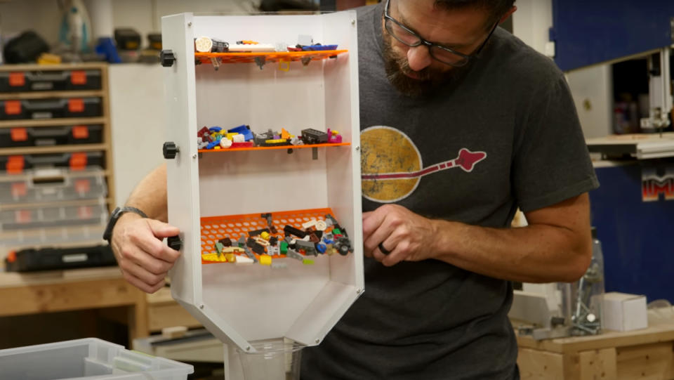 A man using his hands to adjust the orange filters of his DIY LEGO sorter.