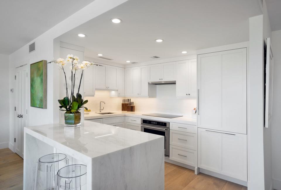 The updated kitchen has white-marble countertops, tile backsplashes, Shaker-style wood cabinetry, and a peninsula with pull-up seating.