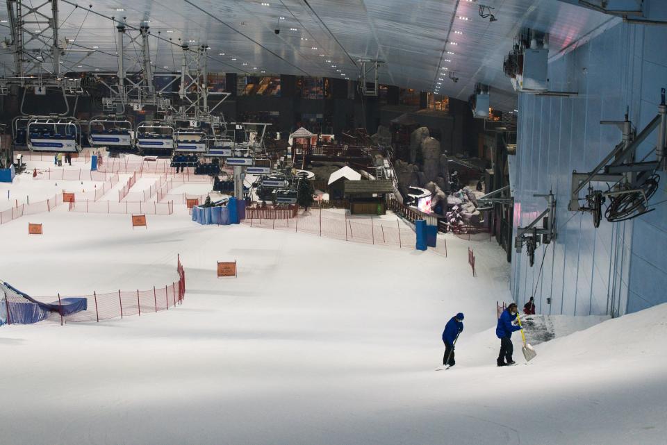 Two employees of Ski Dubai pack snow at Mall of the Emirates in Dubai, United Arab Emirates, Wednesday, May 27, 2020. Dubai on Wednesday loosed its restrictions imposed over the coronavirus pandemic, allowing movie theaters and other attractions to operate. (AP Photo/Jon Gambrell)
