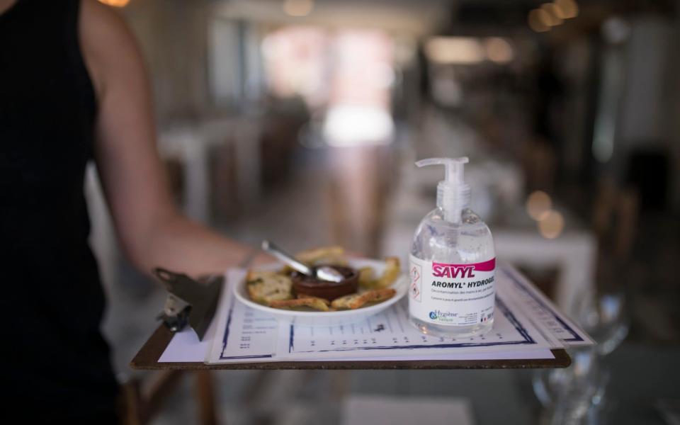 A waitress carries menus and hand sanitiser at a seafood restaurant in Marseille, southern France - AP Photo/Daniel Cole