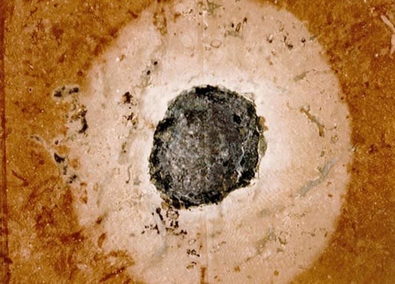 This fossilized meteorite in limestone is typical of those found on Kinnekulle. The black blob in the middle is the meteorite itself, and the grey area around the meteorite is evidence of the reduction process that occurred in the oxidized red