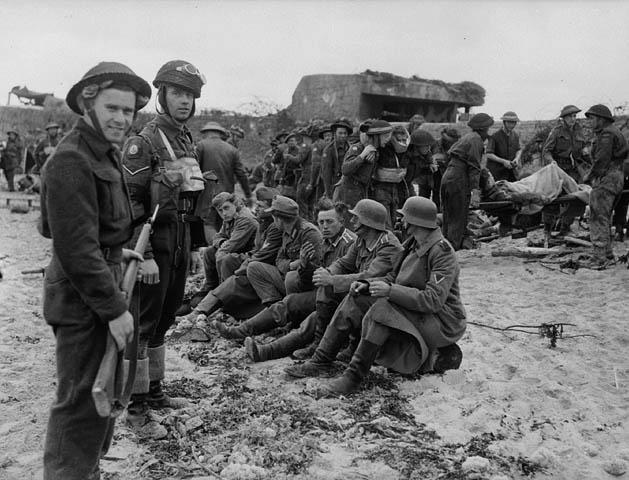 A member of the Canadian Provost Corps (C.P.C.) guarding the first German prisoners to be captured by Canadian soldiers in the Normandy beachhead, France, 6 June 1944.