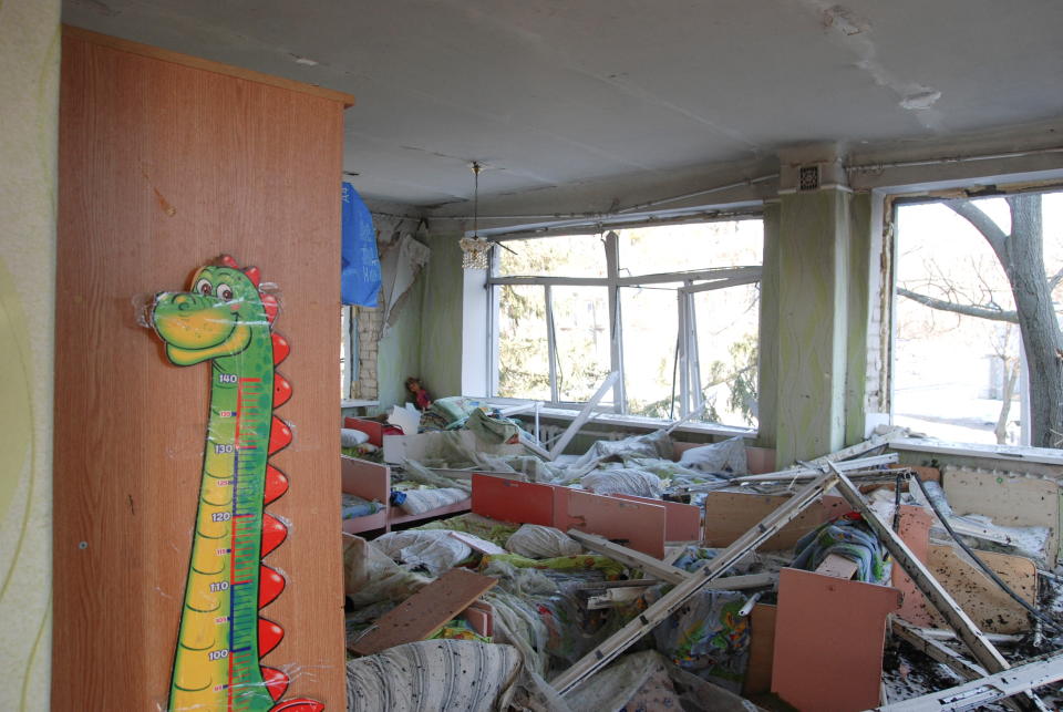 An elementary schoolroom piled with rubble, with a dinosaur height chart intact on a cabinet.