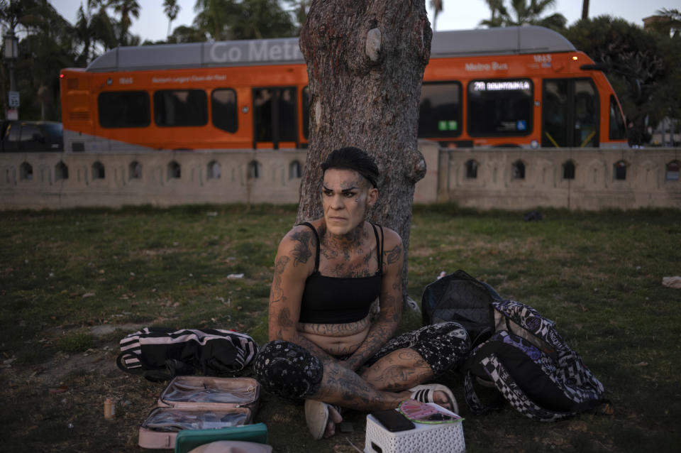 Angel Jesus Gonzalez passes time by a tree after putting on makeup in McArthur Park in Los Angeles, Tuesday, Sept. 19, 2023. There is no single reason why Los Angeles became a magnet for homelessness. Two contributing factors: Soaring housing prices and rents punish those with marginal incomes, and a long string of court decisions made it difficult for officials to clear encampments or relocate homeless people from parks and other public spaces. (AP Photo/Jae C. Hong)