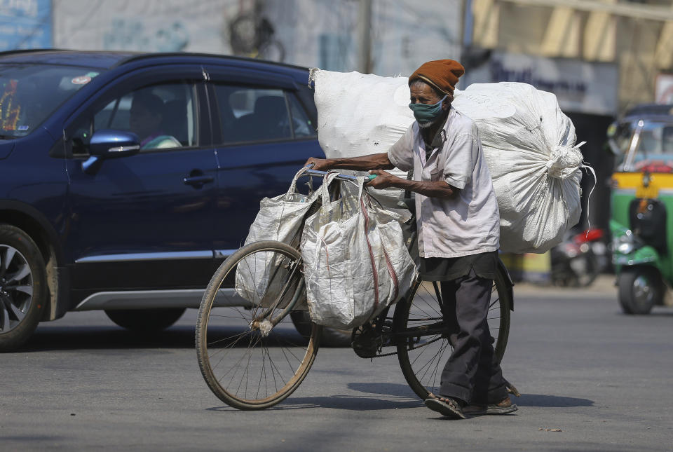 An Indian man wearing face mask as a precaution against the coronavirus pushes his bicycle with load in Hyderabad, India, Thursday, Dec. 17, 2020. (AP Photo/Mahesh Kumar A.)