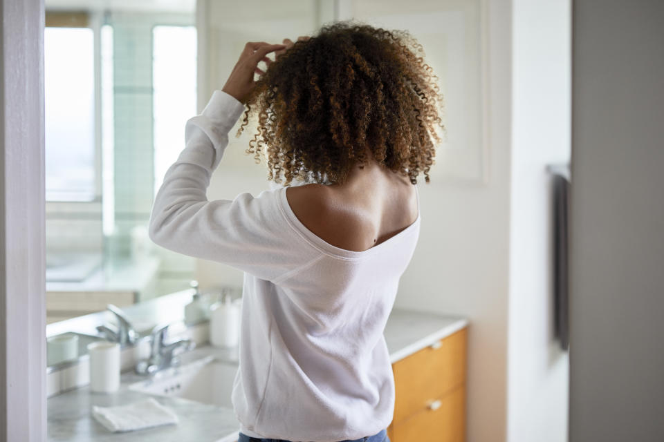 Side view of woman looking in mirror while standing at home