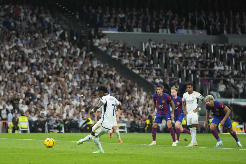 Real Madrid's Vinicius Junior scores on a penalty kick his side's opening goal during the Spanish La Liga soccer match between Real Madrid and Barcelona at the Santiago Bernabeu stadium in Madrid, Spain, Sunday, April 21, 2024. (AP Photo/Manu Fernandez)