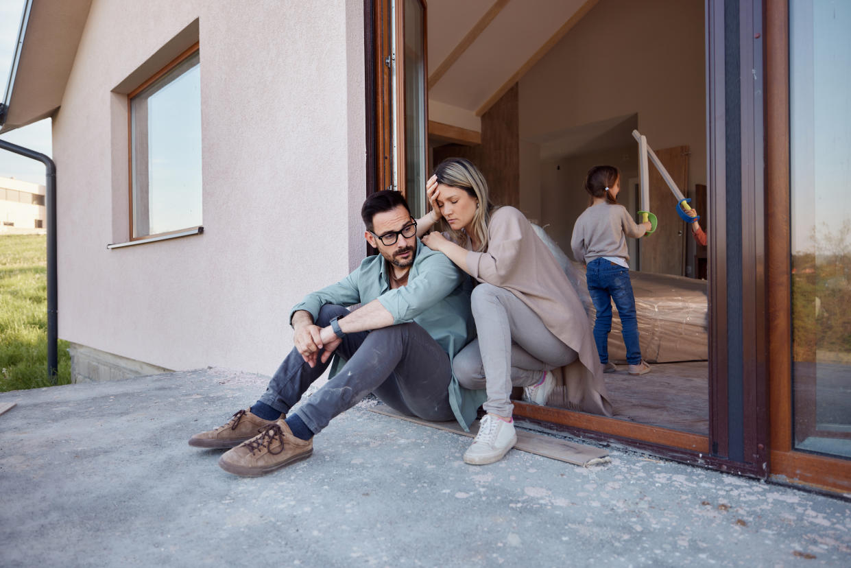 Displeased parents feeling tired on the door of their renovating house while their kids are playing inside.