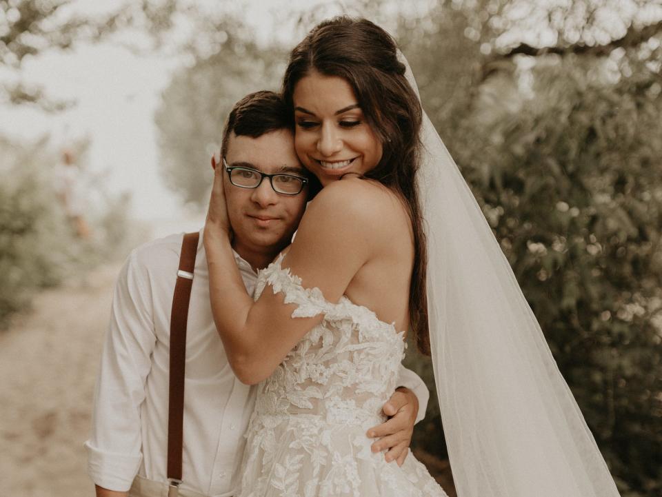 A bride hugs her brother on a beach.