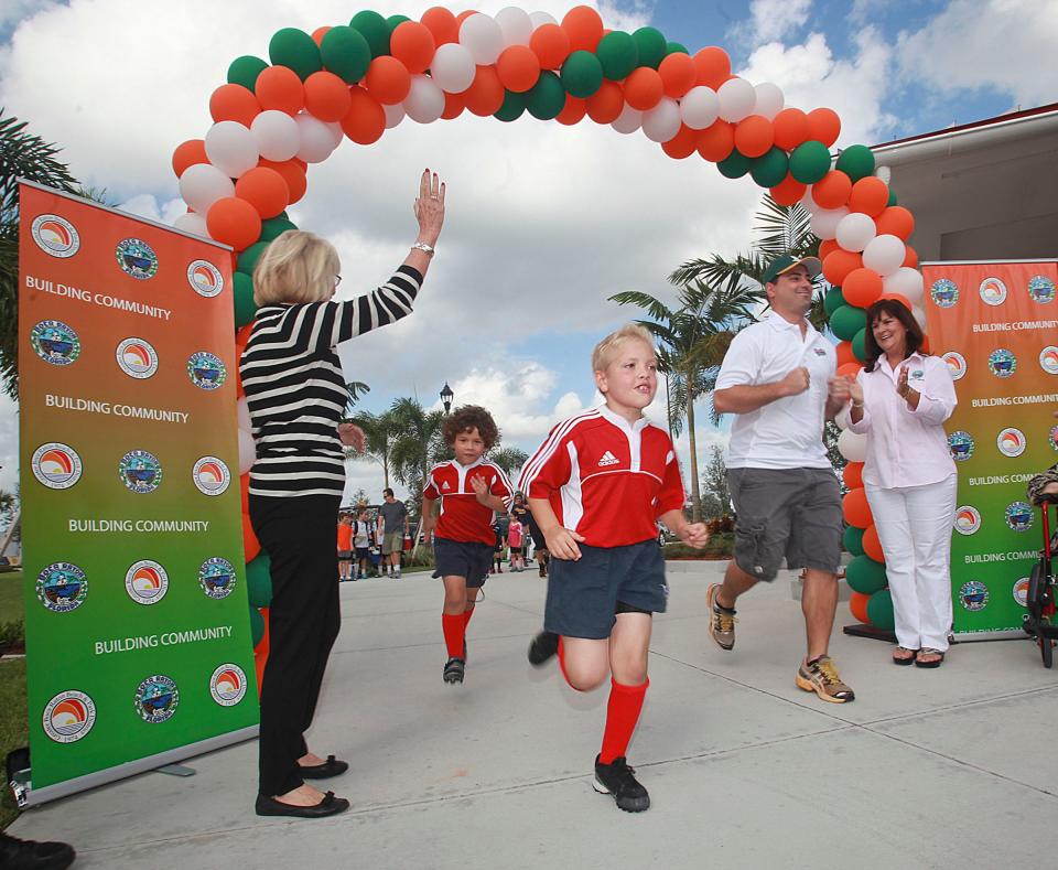 After high-fiving Boca Raton Mayor Susan Whelchel, seven year-old Jaxson Patterson, a member of the Boca Raton Junior Buccaneers rugby team, bursts through and archway made of balloons to help commemorate the Opening Day of The Spanish River Athletic Facilities at de Hoernle Park in 2012.