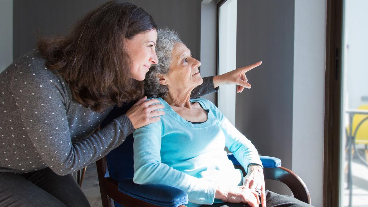 Adult daughter showing to senior mother scene out of window.