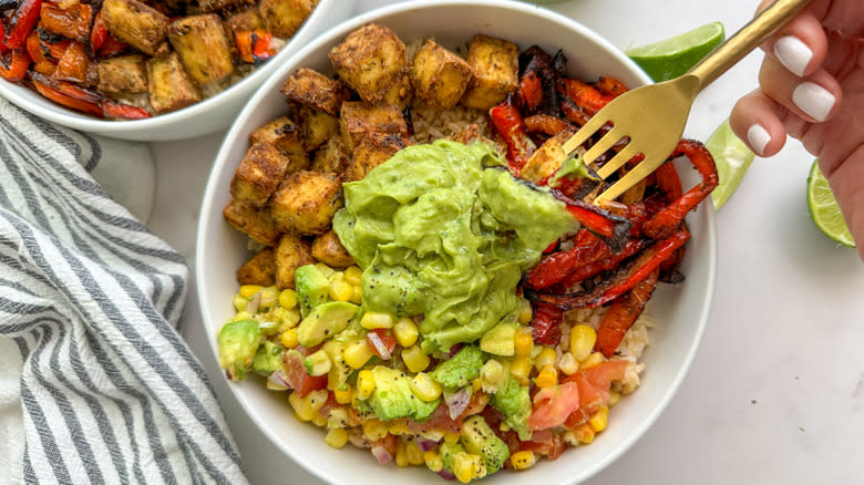 hand with fork in tofu bowl