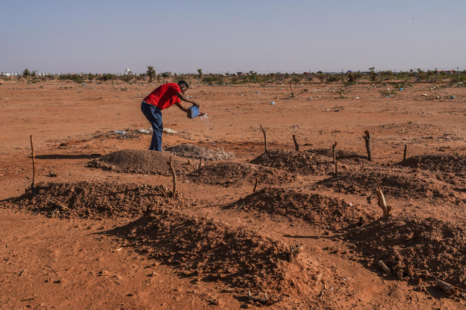 At a children's burial ground, a local aid worker douses a water offering onto the grave of a 2-year-old girl, Iqra, who died from complications due to malnutrition the day before, in Doolow, Somalia. 