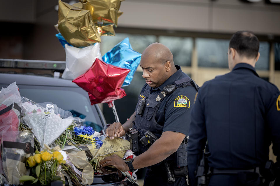 St. Paul Police Officer Anthony Buckley places a badge on a police vehicle that has become one of three memorials in front of the Burnsville Police Department in Burnsville, Minn., Monday, Feb. 19, 2024. Two police officers and a first responder were shot and killed early Sunday and a third officer was injured at a suburban Minneapolis home in an exchange of gunfire while responding to a call involving an armed man who had barricaded himself inside with family. (Elizabeth Flores/Star Tribune via AP)