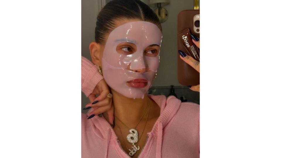 Hailey Bieber shares a mirror selfie of herself wearing a pink jumper and a matching face mask