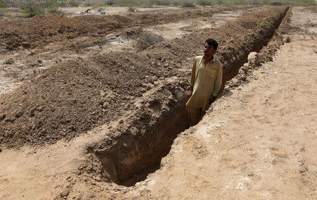 Shahid Balouch, a gravedigger, poses for a photograph in a mass grave in the cemetary, as preparations are made in case of another heatwave in Karachi, Pakistan May 13, 2016. REUTERS/Akhtar Soomro