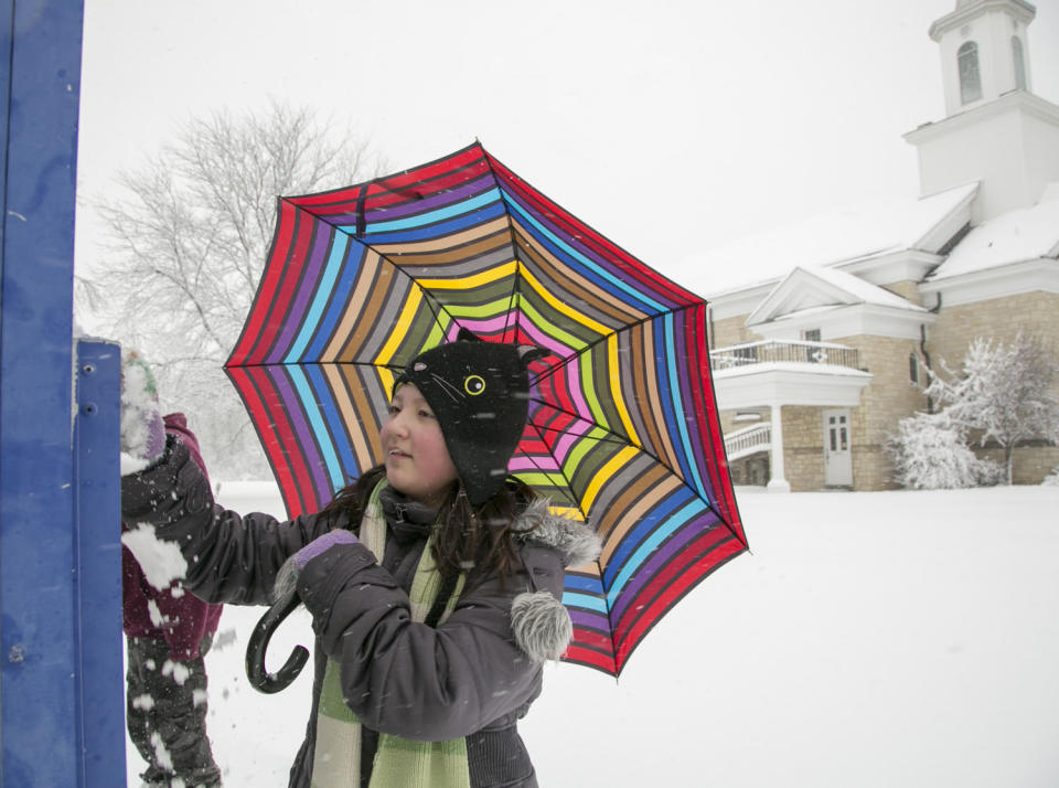 Hana Quinn, 10, wipes snow off the sign for the First Christian Church on South Calhoun Street as she holds her umbrella against the falling snow, Fort Wayne, Ind., Wednesday, March 12, 2014. (AP Photo/The Journal Gazette, Chad Ryan)