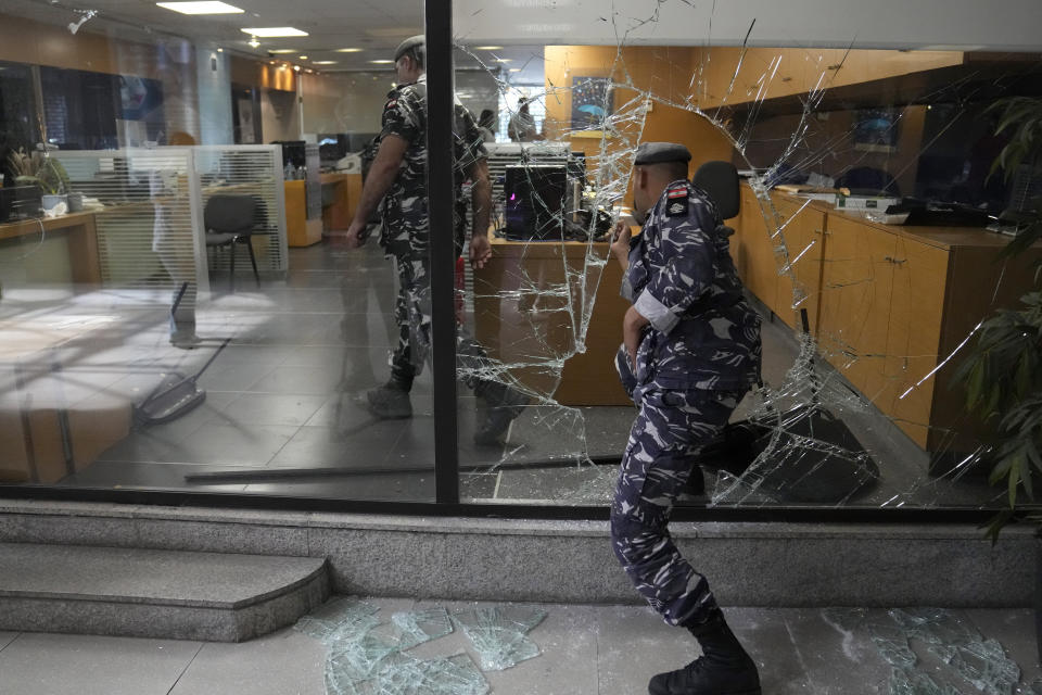 Lebanese policemen enter a bank from a window that was broken by depositors to exit the bank after trying to get their money, in Beirut, Lebanon, Wednesday, Sept. 14, 2022. An armed woman and a dozen activists broke into a Beirut bank branch on Wednesday, taking over $13,000 from what she says were from her trapped savings. Lebanon's cash-strapped banks since 2019 have imposed strict limits on withdrawals of foreign currency, tying up the savings of millions of people. (AP Photo/Hussein Malla)