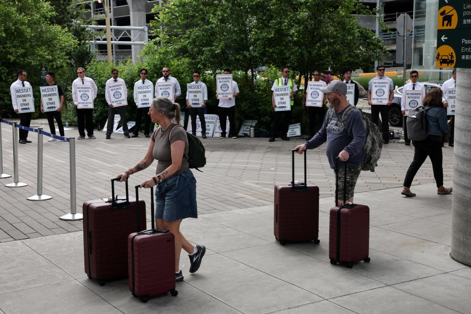 People push luggage past aircraft maintenance engineers and technical staff picketing against WestJet Airlines at Vancouver International Airport on June 29, 2024.