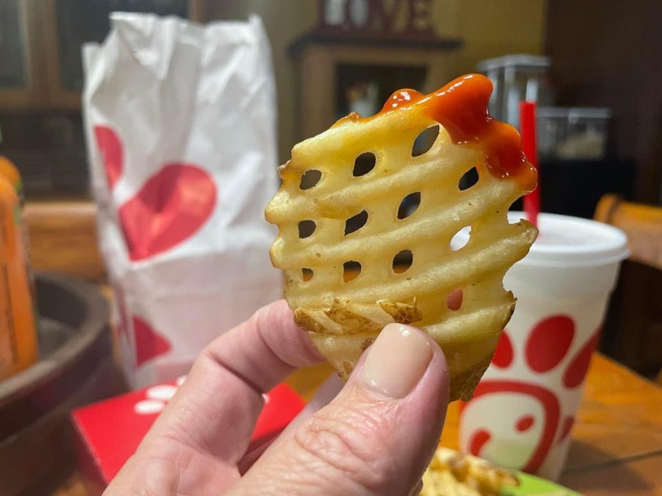 The writer holds a waffle fry dipped in ketchup in front of Chick-fil-A bag and cup